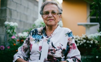 Elderly woman in floral shirt sits on walker.